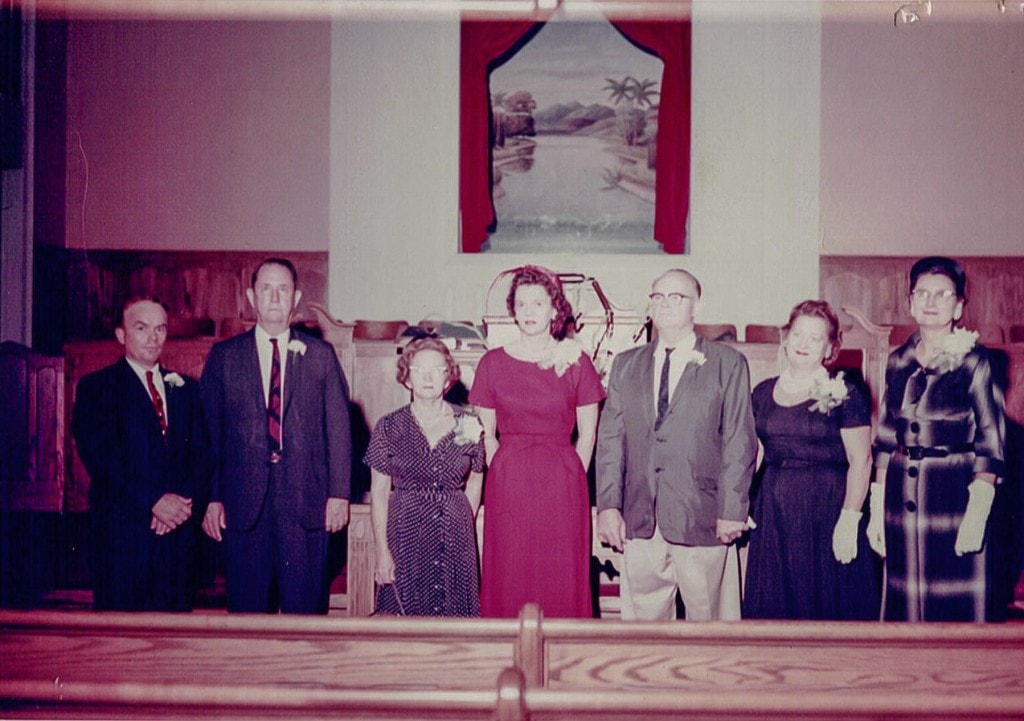 A small group of older members standing in the sanctuary, with empty pews behind them.