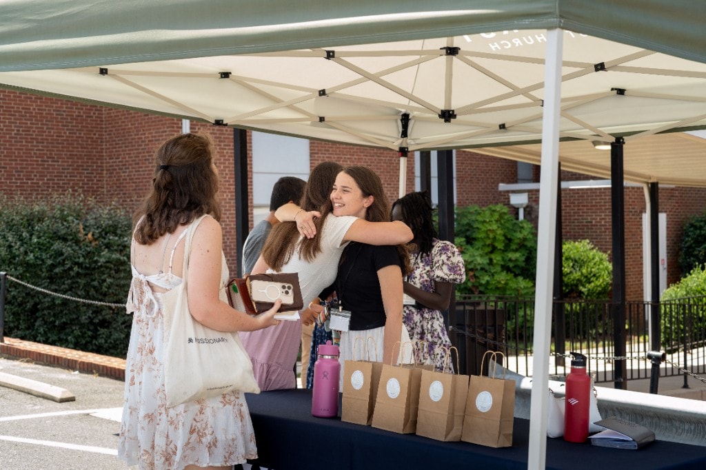 Young people greeting one another under a tent outside the church.